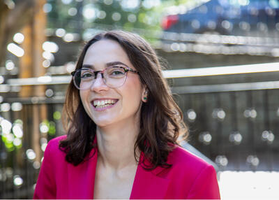 Aliza Adler smiles at the camera while wearing a pink blazer and glasses